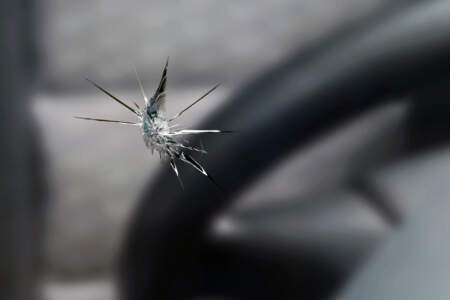 Nahaufnahme eines sternförmigen Steinschlags in der Windschutzscheibe; im Hintergrund ist ein Auto unscharf zu sehen.