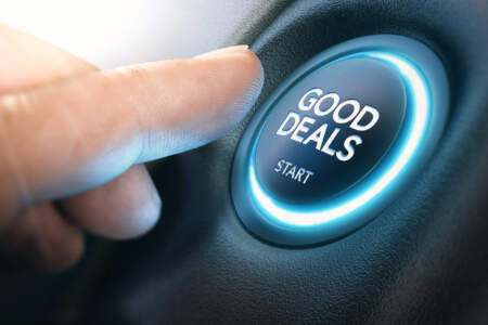 Nahaufnahme eines Fingers, der einen beleuchteten runden Button mit der Aufschrift „GOOD DEALS – START“ drückt.